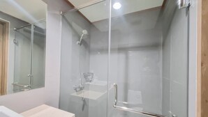 A modern bathroom with a glass-enclosed shower, a vanity with a sink, and a mirror. - Warm And Minimalist Studio Apartment At Patraland Amarta (Ngaglik)