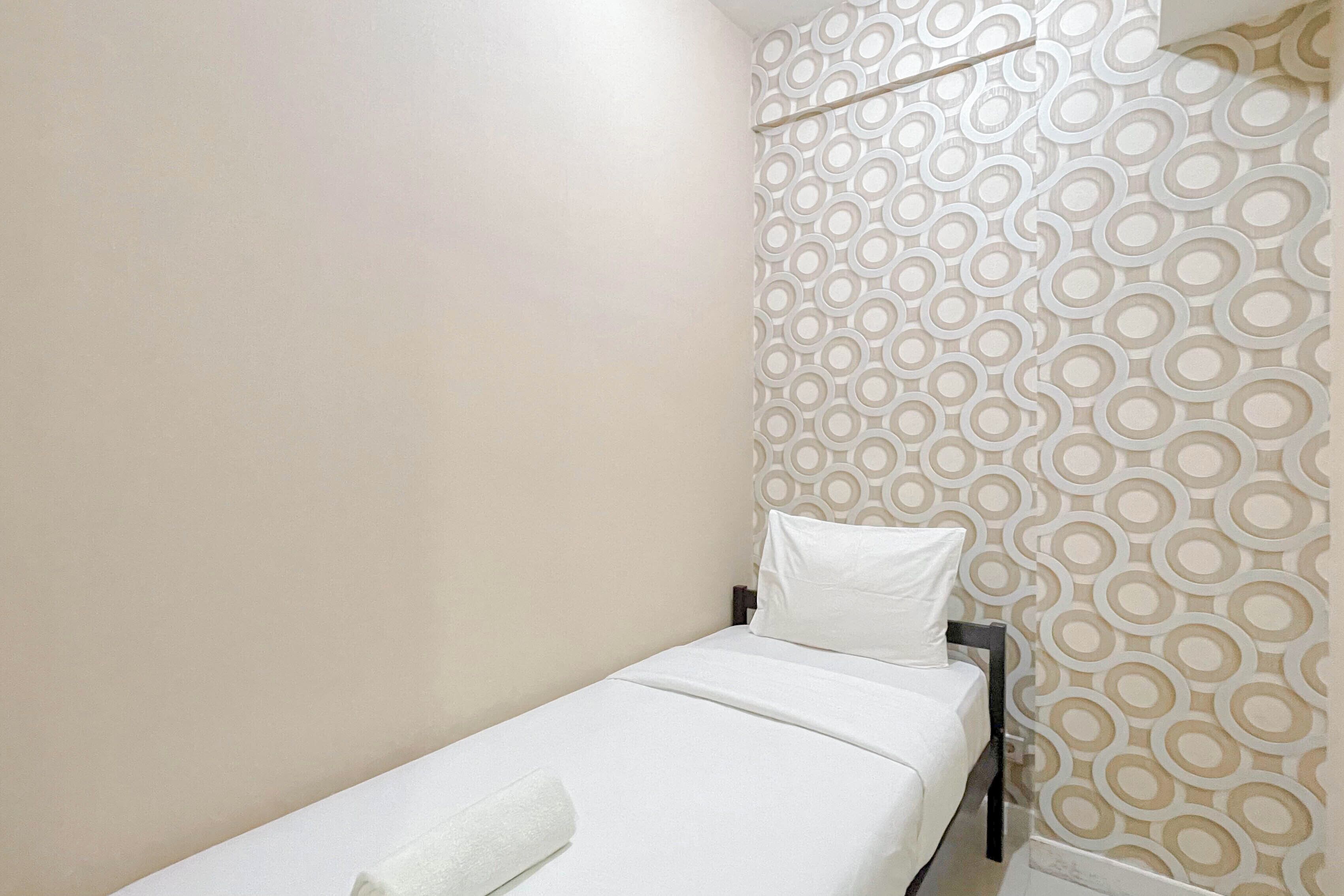 A small, single-bed room with a plain wall and a patterned wallpaper on one side.
