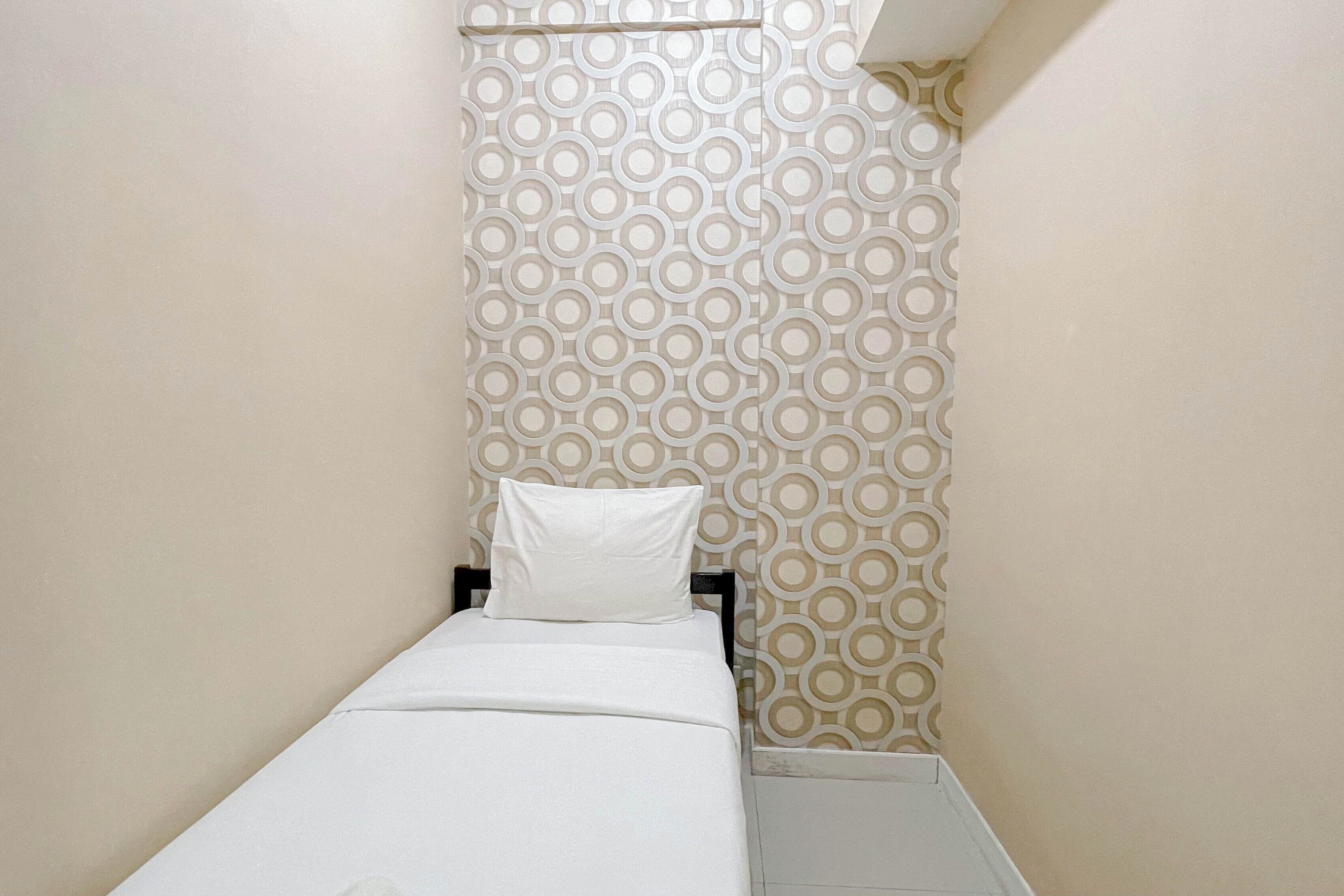 A small, single-bed room with a patterned wallpaper, a white bedspread, and a white pillow.
