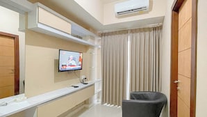A modern hotel room with a mounted TV, air conditioning, a vanity with a mirror, and a window with curtains. - Simple Style 2Br Apartment Vida View Makassar (Makassar)