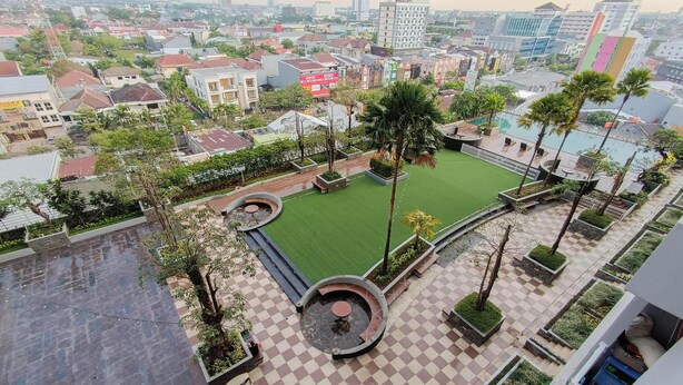 A rooftop garden with a checkered floor, surrounded by palm trees and a green lawn. - Simple Style 2Br Apartment Vida View Makassar (Makassar)