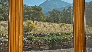 A view through a window with a stone wall and greenery, overlooking a mountainous landscape. - White Lotus House - 2 BR, 2.5 Bath Luxury Sanctuary in Crestone, Colorado (Crestone)