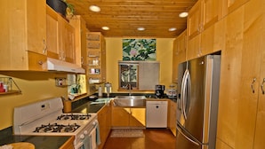 A compact kitchen with wooden cabinets, a gas stove, a stainless steel refrigerator, and a window with a view of greenery. - White Lotus House - 2 BR, 2.5 Bath Luxury Sanctuary in Crestone, Colorado (Crestone)