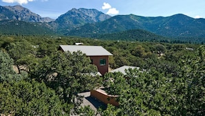 A small building with a sloped roof surrounded by dense greenery and mountains in the background. - White Lotus House - 2 BR, 2.5 Bath Luxury Sanctuary in Crestone, Colorado (Crestone)