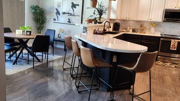 A modern kitchen with a large island, bar stools, and a dining area with a table and chairs.