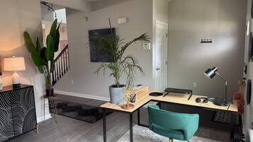 Una sala de estar moderna con un escritorio de madera, una silla color turquesa y una escalera que sube a otro nivel.