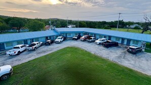 A motel with a blue roof and a parking lot filled with various vehicles. - Arrowhead Motel (Burnet)
