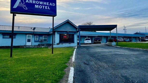 The Arrowhead Motel with a clear entrance, a parking lot, and a blue building facade. - Arrowhead Motel (Burnet)