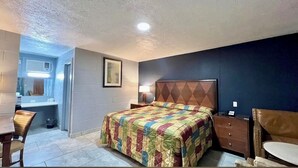 A bedroom with a bed, bedside table, lamp, and a chair. - Arrowhead Motel (Burnet)
