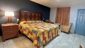 A hotel room with a bed, a nightstand, a chair, a lamp, and a door. - Arrowhead Motel (Burnet)