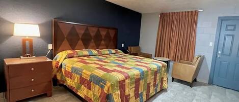 Una camera d'albergo con un letto, un comodino, una sedia, una lampada e una porta.
