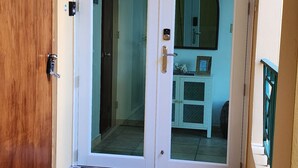 Un pasillo con una puerta de madera, una puerta de vidrio que da a un cuarto con un lavamanos y un armario, y piso de baldosas.