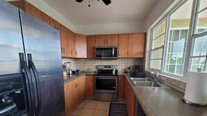 Una cocina moderna con armarios de madera, electrodomésticos de acero inoxidable, un microondas y un amplio ventanal que proporciona luz natural.