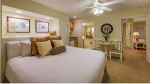 Une chambre d’hôtel avec un grand lit, un ventilateur de plafond, une petite table avec une chaise et une vue sur la salle de bain.