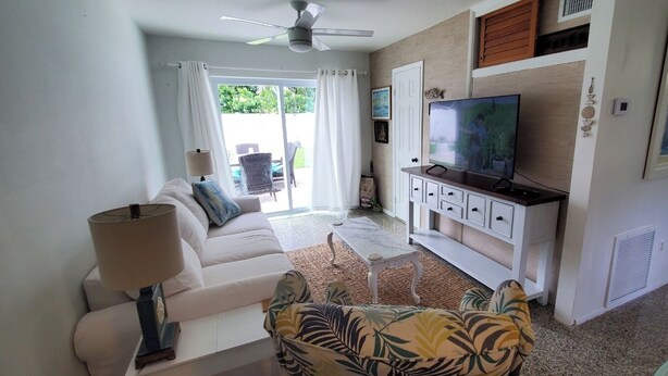 A living room with a white sofa, a patterned armchair, a TV on a white cabinet, and a ceiling fan. - Adorable house with a large private back yard in sunny Vero Beach (Vero Beach)