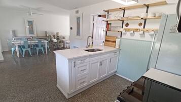 A kitchen with white cabinets, a granite countertop, a sink, and a refrigerator. There is a dining area with a table and chairs in the background.