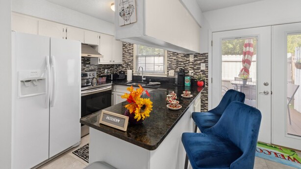 Una cocina moderna con armarios blancos, una encimera negra y una silla azul.