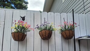 Una cerca de madera blanca con tres macetas colgantes de flores.