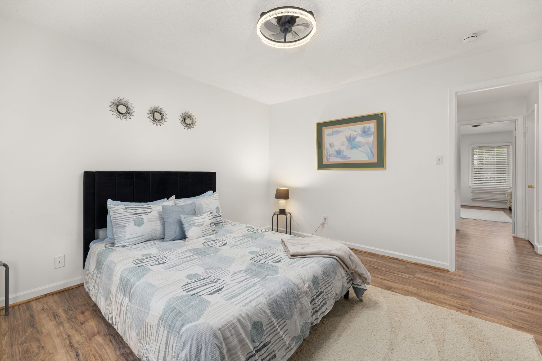 Een slaapkamer met een bed, nachtkastje, lamp en plafondventilator.