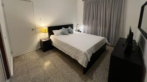 A bedroom with a bed, a ceiling fan, a nightstand, a lamp, a dresser, and a window with curtains. - Marvelous 3-2 house for 6 Big/affordable in Aguadilla (Aguadilla)