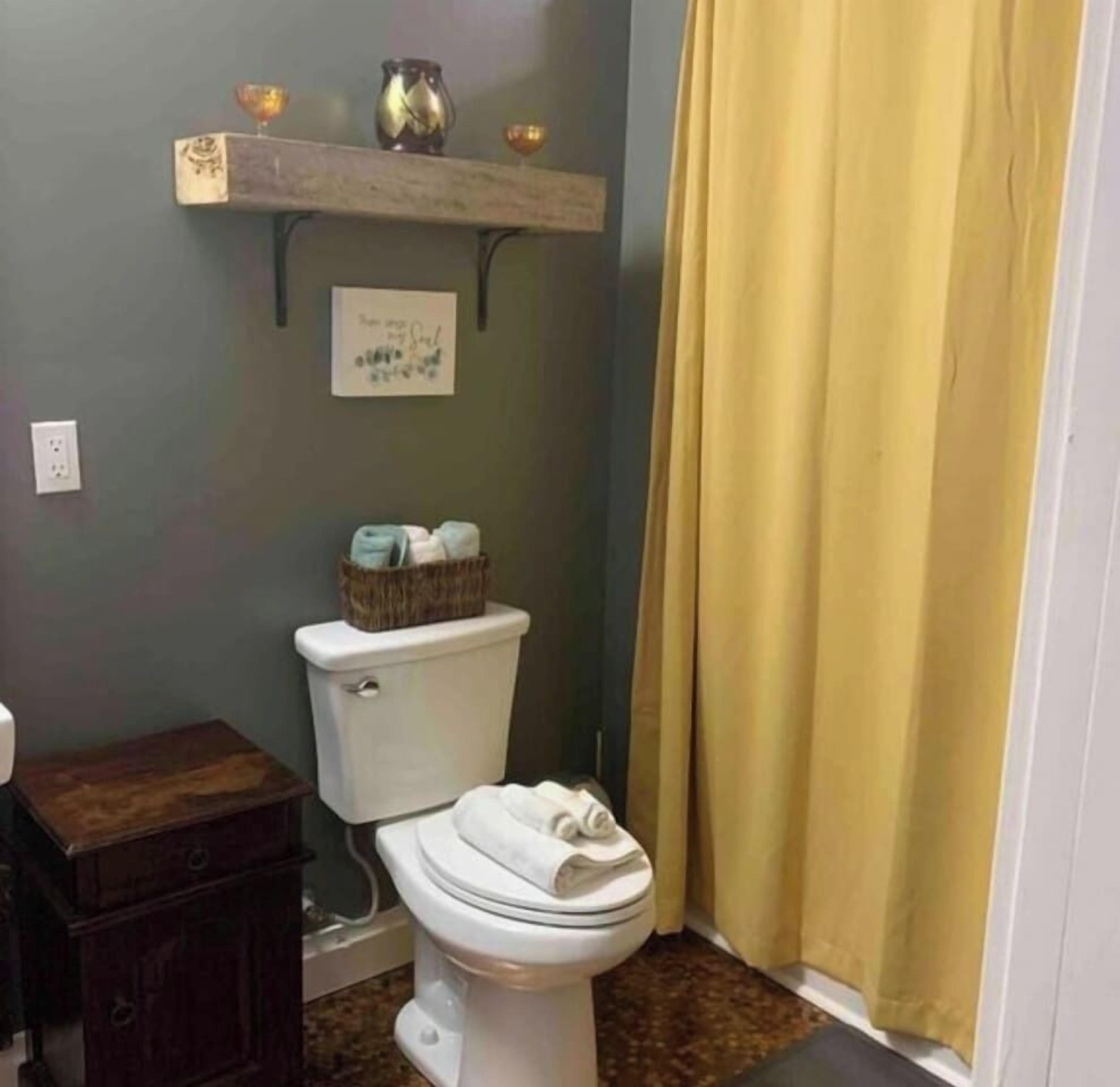 Une salle de bain avec des toilettes, une étagère au-dessus et un rideau jaune.