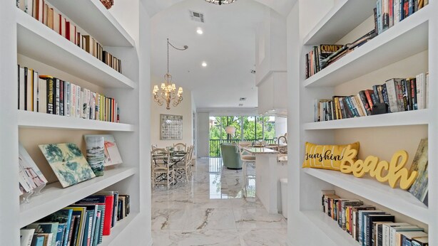 A hallway with bookshelves on both sides, a chandelier, and a view into a dining area. - Ft. Myers Beach Escape | Pool + Canal Views (Fort Myers Beach)