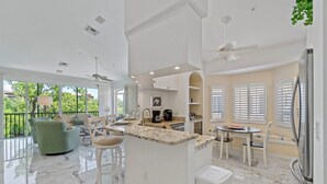 A modern kitchen with a marble countertop, white cabinetry, and a dining area with a table and chairs. - Ft. Myers Beach Escape | Pool + Canal Views (Fort Myers Beach)