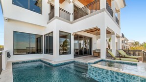 Une maison moderne à deux étages, dotée d’une piscine, de grandes fenêtres et d’un espace salon extérieur.