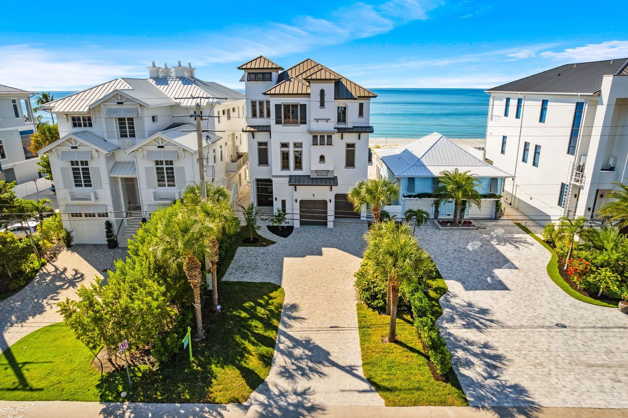 Une propriété située en bord de mer, composée de plusieurs bâtiments blancs, d’une allée pavée et de palmiers.