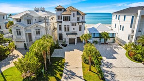 Une propriété située en bord de mer, composée de plusieurs bâtiments blancs, d’une allée pavée et de palmiers.