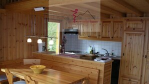 A wooden cabin interior with a kitchen area, wooden dining table, and chairs. - Nice new chalet for rent in Les Collons (Vex)