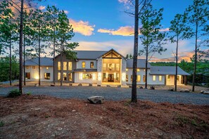 A modern two-story house with a large front porch, surrounded by trees and a gravel driveway. - Iron Bull | Unforgettable Cabin w/ Hot Tub, Games & Mechanical Bull Adventure (Broken Bow)