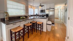A modern kitchen with a central island, bar stools, a ceiling fan, and a microwave. - Pet Friendly 4 Bedroom Just Steps to Beach (Cape May Point)