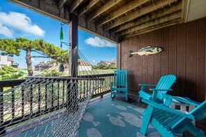 A wooden deck with a hammock, two turquoise Adirondack chairs, and a fish-shaped wall decoration. - Sea Glass Shack - Condo with Hot Tub, Ocean Views and Great Community Amenities! (Kitty Hawk)