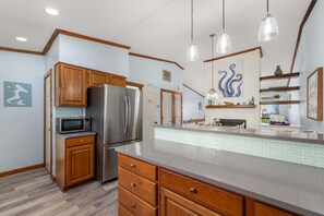 A modern kitchen with wooden cabinets, stainless steel appliances, and a tiled backsplash. - Sea Glass Shack - Condo with Hot Tub, Ocean Views and Great Community Amenities! (Kitty Hawk)