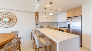 A modern kitchen with a central island, bar stools, a stainless steel refrigerator, and pendant lighting. - Mar del Plata 5B (Bucerías)