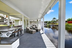Eine überdachte Terrasse im Freien mit Essbereich, Sitzgelegenheiten und Blick auf ein Gewässer.