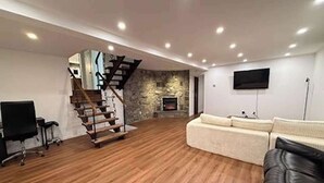 Ein großzügiger Wohnbereich mit Holzboden, einer Treppe, einem Flachbildfernseher und einem Sofa.