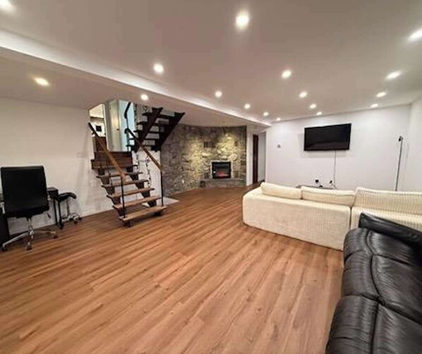 A spacious living area with a wooden floor, a staircase, a flat-screen TV, and a sofa. - Monticello Family Retreat. Pool, Firepit. 7min to casino. Sleeps 15 (Monticello)