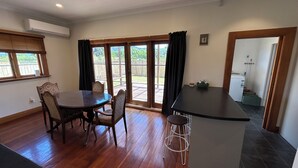 Un espace repas avec une table et des chaises, un coin bar avec des tabourets, et une vue sur une terrasse extérieure accessible par de grandes portes-fenêtres coulissantes.