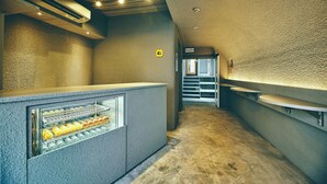 A narrow hallway with a reception desk, a refrigerated display case, and a counter with a sink. - HOTEL URO - hostel (Nagasaki)