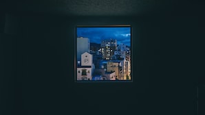 A view through a window of a cityscape at dusk with buildings and a prominent clock tower. - HOTEL URO - hostel (Nagasaki)