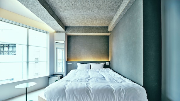 A modern bedroom with a large bed, a round table, and a view of the city through a large window. - HOTEL URO - hostel (Nagasaki)
