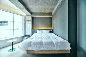 Une chambre moderne avec un grand lit, une table ronde et une vue sur la ville, visible à travers une grande fenêtre.