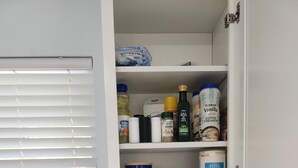 Une cuisine équipée d’une machine à café, d’un placard contenant divers produits alimentaires et d’un plan de travail muni d’un support à capsules de café.