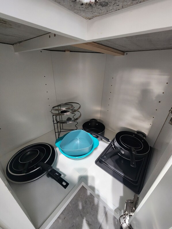 A compact kitchen with a gas stove, a blue colander, a frying pan, and a pot.