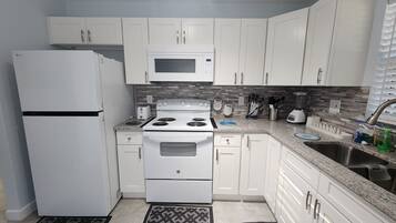 A modern kitchen with white cabinets, a built-in microwave, stove, and refrigerator. There is a sink with a faucet, and various kitchen utensils are visible.