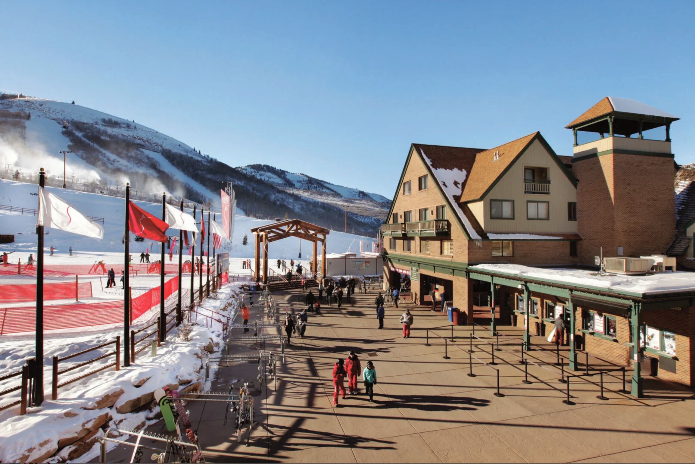 A ski resort with a covered pedestrian area, a mountain backdrop, and a building with a sloped roof.