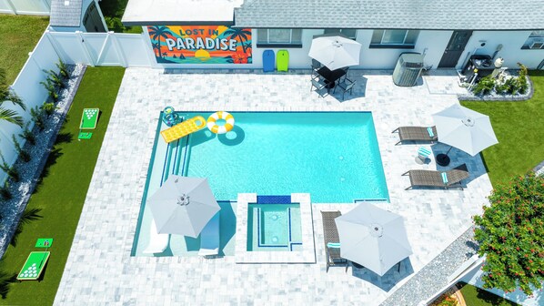 Una piscina con sillones de descanso, sombrillas y mesa de billar.