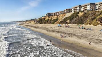 A coastal hotel with multiple floors, a sandy beach, and a rocky cliff.